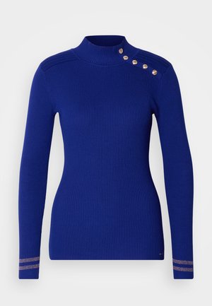 Jersey azul acanalado con cuello alto, mangas largas y detalle de botones dorados en el hombro, con acentos metálicos a rayas en los puños.