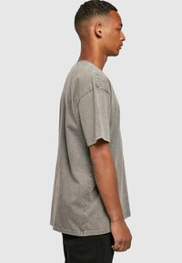 Grijze oversized katoenen T-shirt met korte mouwen, een ronde halslijn en een vervaagde afwerking met zichtbare stikseldetails.