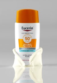 Eucerin sun protection bottle with orange cap, white plastic body, and blue label. Contains ultra-light fluid, SPF 50+, and medical skin details.