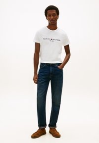 Valge T-särk "Tommy Hilfiger" logoga, tumedasinine teksapüksid, pruunid seemisnahast kingad. Sile tekstuur, vaba lõikega, teksapükstel üles keeratud ääred.