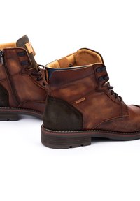 Botas de cuero marrón con cierre de cordones en la parte delantera, cremallera lateral y panel texturizado en contraste, con suela gruesa y detalle de costura.