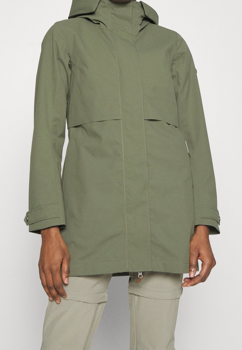 Parka de couleur vert olive, imperméable, avec capuche, fermeture éclair et poignets ajustables par pression. Dispose d'une poche à rabat à l'avant et d'une texture lisse.