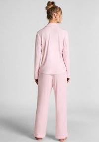 Roze lange mouwen pyjama-top met een kraag, gecombineerd met bijpassende wijde broek, gemaakt van zachte stof. Eenvoudig, naadloos ontwerp.