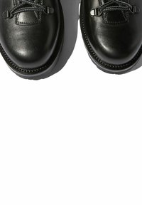 Zapatos de cuero negro con puntas redondeadas, superficie texturizada y cordones resistentes. La suela exterior es blanca, proporcionando un contraste con el diseño superior.