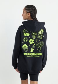 Black hoodie featuring neon green graphics on the back, including various playful doodles and the word "VISUALIZE" at the bottom.