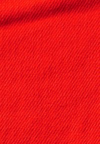 Gros plan d'un tissu rouge vif avec une texture de tissage diagonal et un petit pli ombragé près du coin supérieur gauche.