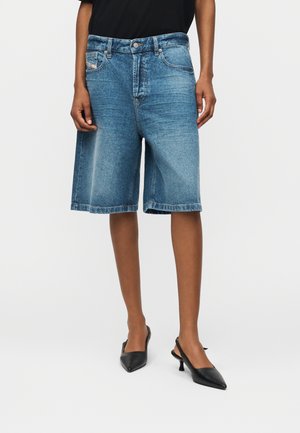 Άτομο που φοράει μπλε τζιν σορτς μήκους μέχρι τη μέση, σε συνδυασμό με μαύρα slingback kitten heels, σε απλό φόντο.