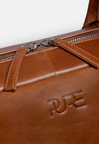 Braune Lederhandtasche mit glatter Textur, ausgestattet mit einem Reißverschluss, Metallbeschlägen und geprägt "PURE" Logo-Detail.
