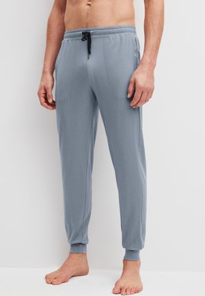 Man draagt lichtblauwe joggingbroek met elastische tailleband en zwart trekkoord, staat blootsvoets tegen een effen achtergrond.