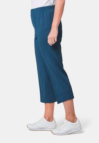 Teal cropped broek met een brede elastische tailleband, met zijslits aan de zoom. Gecombineerd met witte sneakers voor een casual uitstraling.