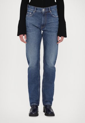 Jeanși din denim albastru cu croială dreaptă, design cu cinci buzunare, estompare subtilă și cusături în contrast. Purtați cu un top negru cu textură, cu mânecă lungă.