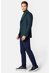 Granatowe bawełniane spodnie w połączeniu z ciemnozieloną marynarką w kratę i zielonym golfem, dopełnione teksturowanymi granatowymi trampkami.