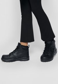 Black high-top sneakers featuring a smooth leather upper, round laces, textured rubber outsole, and a subtle branding accent on the side.