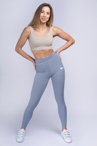 Leggings grigie chiare con vita alta e logo ricamato, abbinate a un crop top beige. L'outfit è completato da sneakers bianche.