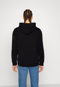 Felpa nera con un grande cappuccio, realizzata in tessuto morbido, con polsini e orlo a costine, indossata con jeans in denim azzurro chiaro.