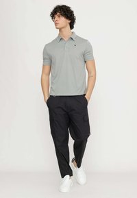 Polo grigio chiaro con colletto e logo, abbinato a pantaloni cargo neri con tasche laterali, completato da sneakers bianche.