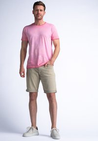 Camiseta de algodón rosa claro con mangas cortas, combinada con pantalones cortos beige arremangados. Complementada con zapatillas blancas con un acento negro.