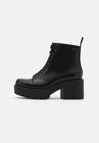 Botas de cuero negras hasta el tobillo con una suela de plataforma gruesa y texturizada. Presentan puntera redonda, cordones con ojales y una lengüeta en la parte trasera.