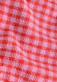 Textil med ett vävt mönster av växelvis ljusrosa och korallröda rutor med zick-zack-texturer, vilket skapar en taktil yta som tilltalar.