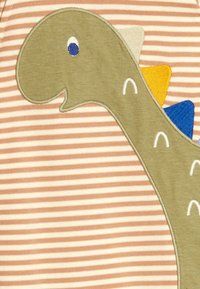 Applique di un dinosauro verde con un sorriso su uno sfondo rigato pesca e bianco, con spine blu, gialle e bianche. Texture morbida.