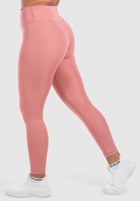 Leggings atletici rosa a vita alta, caratterizzati da una texture liscia e un design aderente. Indossati con sneakers bianche per un look attivo.