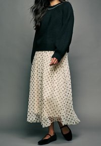 Un pull en maille noire avec une coupe décontractée, associé à une jupe maxi à pois crème et des ballerines noires, mettant en valeur un style superposé.