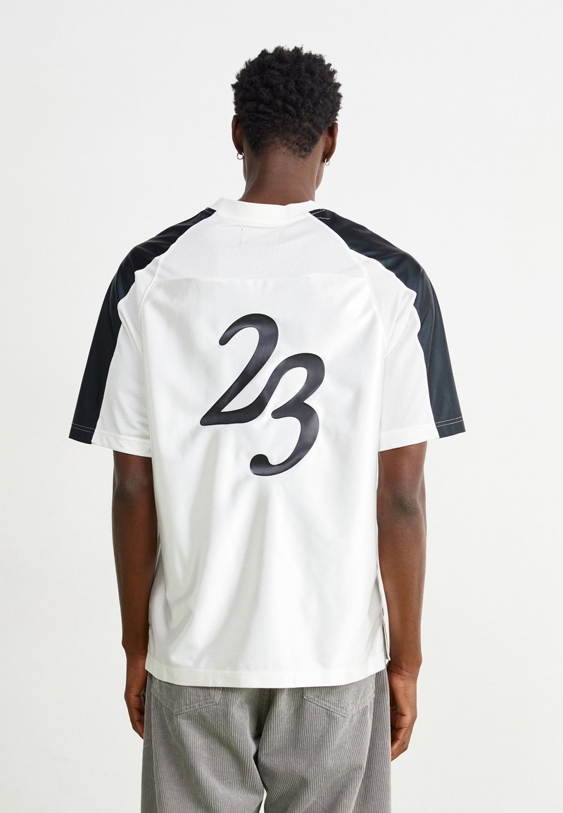 Kortsleeve jersey med hvit kropp og svarte detaljer på skuldrene, med et stort svart "23" trykket på baksiden. Mesh tekstur synlig.