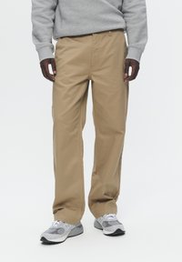 Pantaloni kaki din bumbac, cu un croi lejer și buzunare laterale. Purtați cu pantofi sport gri și un hanorac gri deschis.
