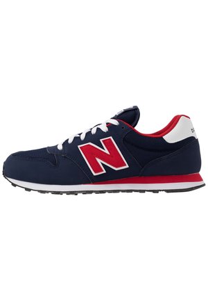 Zapatilla deportiva azul marino con logo "N" rojo, cordones blancos, suela roja y blanca, y forro interior rojo, mostrada de perfil.