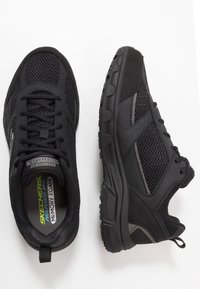 Schwarze Sportschuhe mit Mesh- und synthetischem Obermaterial, strukturierten Überzügen, gepolstertem Kragen und einer strapazierfähigen Gummisohle. Entwickelt für Komfort und Unterstützung.