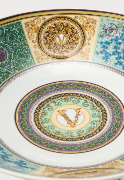 Πορσελάνινο πιάτο με περίτεχνα πολύχρωμα λουλουδένια και αμπελώδη σχέδια, με κεντρικό χρυσό γράμμα "V" περιβαλλόμενο από διακοσμητικά πλαίσια.