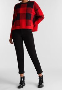 Jersey de punto a cuadros rojo y negro con mangas largas, combinado con jeans ajustados negros y botas de combate negras brillantes con cordones.
