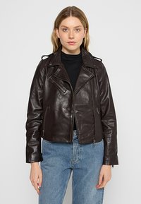 Bruine leren cropped bikerjack met ritssluiting aan de voorkant, diagonale borstzak en dubbele kraag, gecombineerd met lichtblauwe denim jeans.