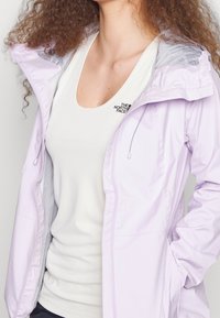 Svetle fialová, voděodolná bunda se zipem vpředu a stažitelnou kapucí, nošena přes bílý tílko. Obsahuje síťovou podšívku.