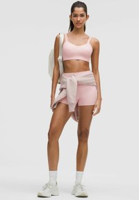 Pink athletic crop top with adjustable straps paired with pink shorts. A light sweater tied at the waist and white sneakers complete the outfit.