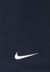 Granatowa tkanina sportowa z białym logo Nike w kształcie prz swoosh, gładka tekstura oraz kontrastowe przeszycia wzdłuż dołu.