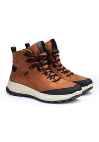 Bottes de randonnée en cuir marron avec des accents textiles noirs, lacets ronds et semelle rembourrée de couleur crème. Dotées d'une languette de traction à l'arrière.