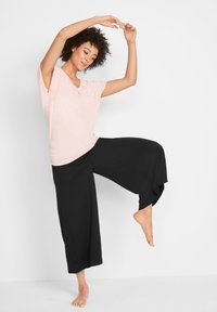 T-shirt rosa chiaro a maniche corte e scollatura a V, abbinato a pantaloni neri a gamba larga. Tessuti morbidi, design casual.