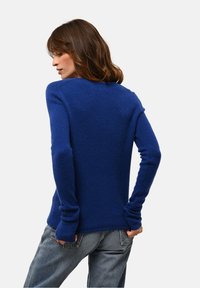 Blauer Strickpullover mit langen Ärmeln, runder Ausschnitt und weicher Textur. Getragen mit lockeren, verblassten Jeans.