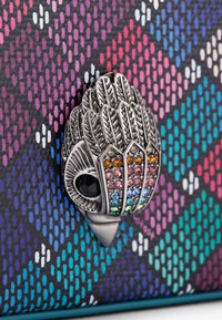 Metalen accent met een gedetailleerd bladontwerp en multicolore rhinestones op een patroon van zwart, teal en roze achtergrond.