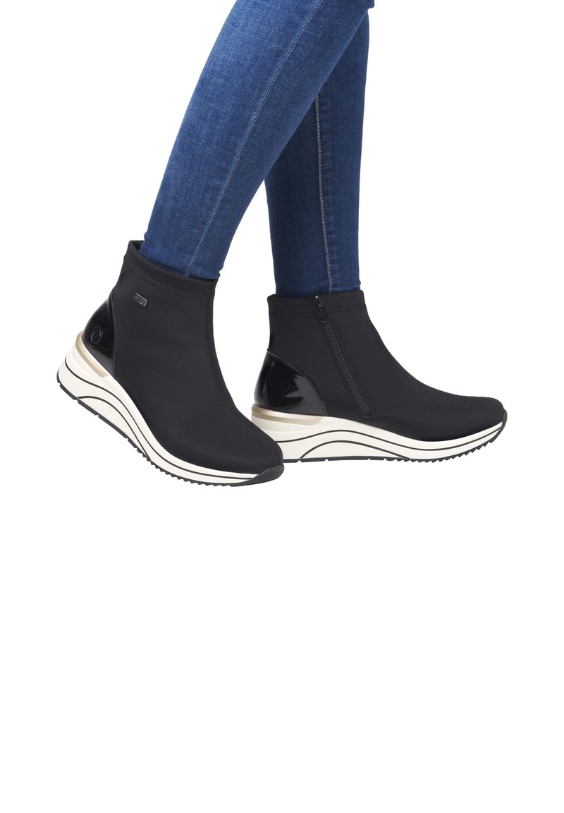 Schwarze Stiefeletten aus elastischem Material mit einem seitlichen Reißverschluss, ausgestattet mit einer weißen, geschichteten Wedge-Sohle und schwarzen, glänzenden Akzenten.