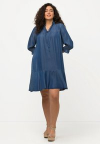 Denimmekko rentoa istuvuutta, röyhelökaulusta ja pitkiä hihoja. Ominaisuuksiin kuuluu kerroksellinen muotoilu ja kootut hihansuut. Väri: tummansininen.