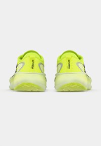 Neon yellow athletic shoes with black accents, featuring a cushioned sole and textured grip. Reflective logo detail on the sides.