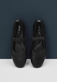Zwarte ballerina's met een ronde neus, voorzien van een ruche-accent rond de enkelband en een gladde, matte afwerking.