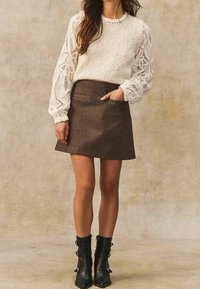 Kremowy sweter dziany z koronkowymi rękawami, w połączeniu z brązową spódnicą w kratę z kieszeniami. Całość dopełniają czarne botki za kostkę z klamrami.