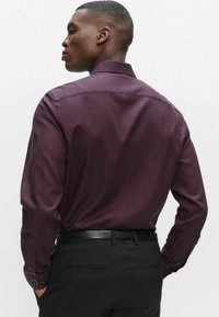 Langærmet skjorte i mørk bordeaux med subtilternet mønster, letvægtsstof, knapmanchetter og en spredt krave, kombineret med sorte bukser.