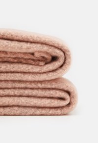 Deux couvertures en laine rose pâle, soigneusement pliées, empilées sur une surface blanche.