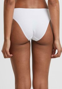 String en coton blanc avec une texture lisse, présentant une coupe taille basse et une couverture arrière minimale. Pas de coutures visibles ni d'ornements.