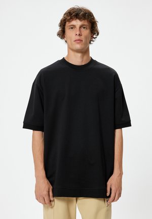 Camiseta negra de gran tamaño hecha de algodón suave, con un cuello redondo y mangas cortas arremangadas, con un dobladillo recto y sin patrones visibles.
