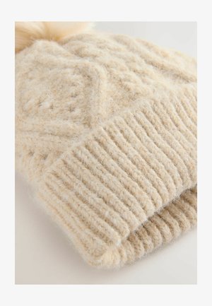 Weiche, cremefarbene Strickmütze mit strukturiertem Zopfstrickmuster und geripptem Bündchen. Oben mit einem flauschigen Bommel verziert.